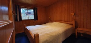 Ein Zimmer mit Holzwänden, einem Einzelbett, einem fenster mit Vorhängen und einer Holzbank.