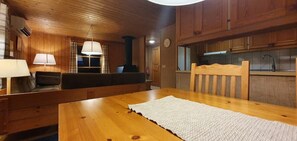A wooden interior with a dining table, sofa, lamps, and a kitchen area.