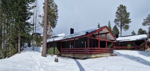 A cabin with a red roof and green exterior, surrounded by snow-covered ground and trees.