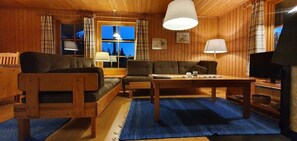 Ein Holzblockhaus-Innenraum mit einer Sofagarnitur, einem Couchtisch, einem Fernseher und einem Fenster mit Vorhängen.