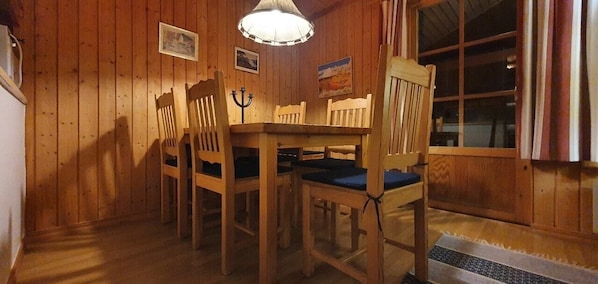 Ein Esszimmer mit Holzboden, einem Tisch und Stühlen, einer Hängelampe und einem Fenster mit Vorhängen.