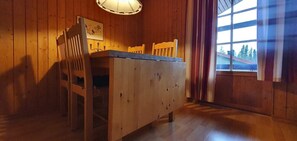 Ein Holztisch mit Stühlen, eine Pendelleuchte und ein Fenster mit Vorhängen.