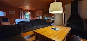 Ein gemütliches Blockhaus-Interieur mit Esstisch aus Holz, einer Couch und einem Kamin.