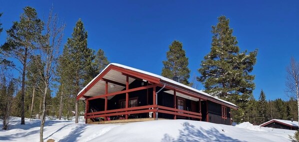Eine Hütte mit roter Fassade, großen Fenstern und verschneiter Landschaft.