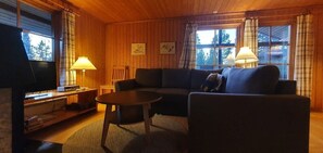 Ein gemütliches Blockhauss-Interieur mit Sofa, kleinem Tisch, Fernseher und Lampe.
