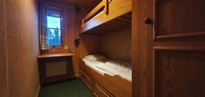 Ein Schlafraum mit Etagenbetten, einem Fenster, einer Heizung und Holzwänden.