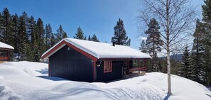 Eine Hütte mit schneebedecktem Dach, umgeben von Bäumen und wolkenlosem Himmel.