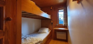 Ein kleiner, kompakter Raum mit einem Etagenbett, einem kleinen Schreibtisch und einem Fenster.