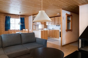 A cozy living room with a sofa, a round table, and a kitchen area with wooden cabinets and a hanging light fixture.