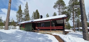 A cabin with a covered porch, surrounded by snow and trees.