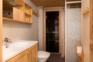 A bathroom with a white sink, wooden cabinets, a toilet, and a shower with a patterned curtain.