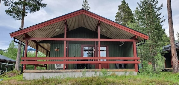 A cabin with a red roof, a porch, and a large window.