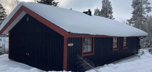 Eine kleine, dunkelholzene Holzhütte mit verschneitem Dach, Schornstein und einer Nummer 77.