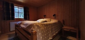 Ein Zimmer mit Holzvertäfelung, einem Bett, einem Fenster mit Vorhängen und einem kleinen Tisch.