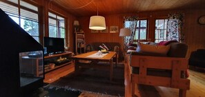 Ein gemütliches Blockhauss-Interieur mit Fernseher, Holzmöbeln und großen Fenstern.
