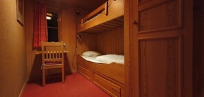 Ein Schlafraum mit Etagenbetten, einem Holztisch und Stuhl, einem roten Teppich und einem Fenster mit rotem Vorhang.