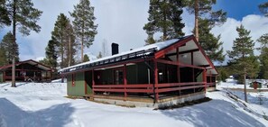 A cabin with a covered porch, a chimney, and a snow-covered landscape.