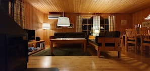 Ein Zimmer mit Holzwänden, einer Couch, einem Tisch, Stühlen und einem Fernseher.