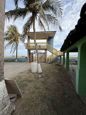 A coastal property with a staircase leading to a covered area, palm trees, and a view of the sea.
