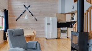 Ein modernes Interieur mit Holzboden, einem grauen Sofa, einem weißen Kühlschrank, einem Herd und einem an der Wand befestigten Skihalter.