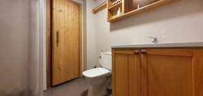 A bathroom with a wooden door, a white toilet, and a wooden vanity with a sink.