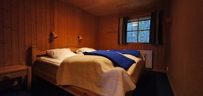 A wooden cabin bedroom with two beds, a window with curtains, and a nightstand.