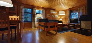 A wooden cabin interior with a sofa, chairs, a television, and a fireplace.