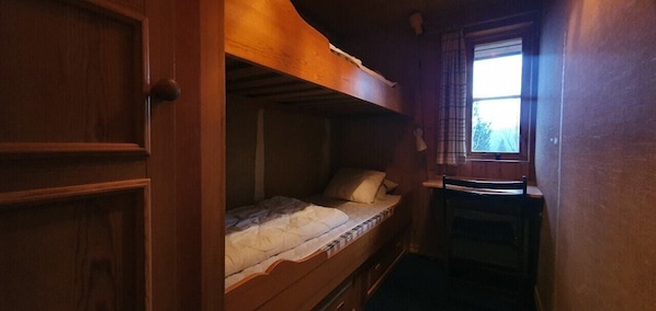 A bunk bed room with a window, wooden walls, and a small table.