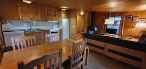 Ein Holzinterieur mit Esstisch, Stühlen, einer Couch, einer Küche mit Schränken und Geräten sowie einem Fernseher.