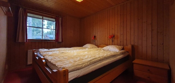 Ein Zimmer mit Holzvertäfelung, einem Bett, einem Vorhangfenster und einer Heizung.