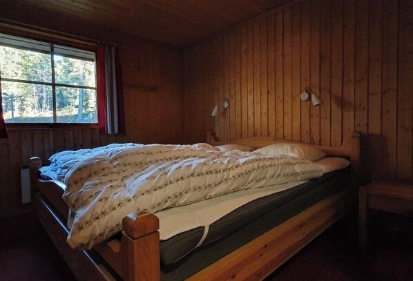 Ein Schlafzimmer einer Holzhütte mit einem Bett, einem Fenster und zwei Wandlampen.