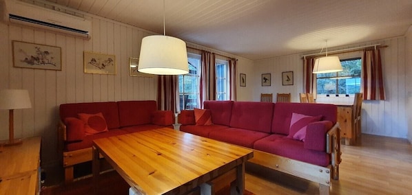 Ein Zimmer mit Holztisch, rotem Sofa und einem Essbereich mit Stühlen.