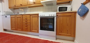 Eine Küche mit Holzausstattung, einem weißen Backofen, einer Mikrowelle und einem roten Teppich.