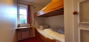 Ein Schlafraum mit Etagenbetten, einem Fenster, einem Schreibtisch und einer Tür.