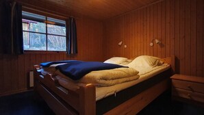 Yhden hengen sänky, jossa on sininen peitto, puiset seinät, ikkuna, jossa on verhot, ja yöpöydällä olevat lamput.