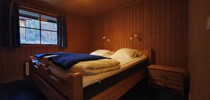 Ein Einzelbett mit blauer Decke, Holzwänden, einem Fenster mit Vorhängen und Nachttischlampen.