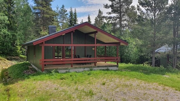 Pieni mökki, jossa on punainen katto ja puuseinät, ja sen ympärillä on puita.