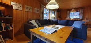 Ein gemütliches Zimmer mit Holzwänden, einem blauen Sofa, einem Holztisch und einem Bücherregal.