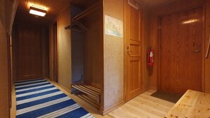 Käytävä, jossa on puinen ovi, sinivalkoraidallinen matto ja puinen penkki.
