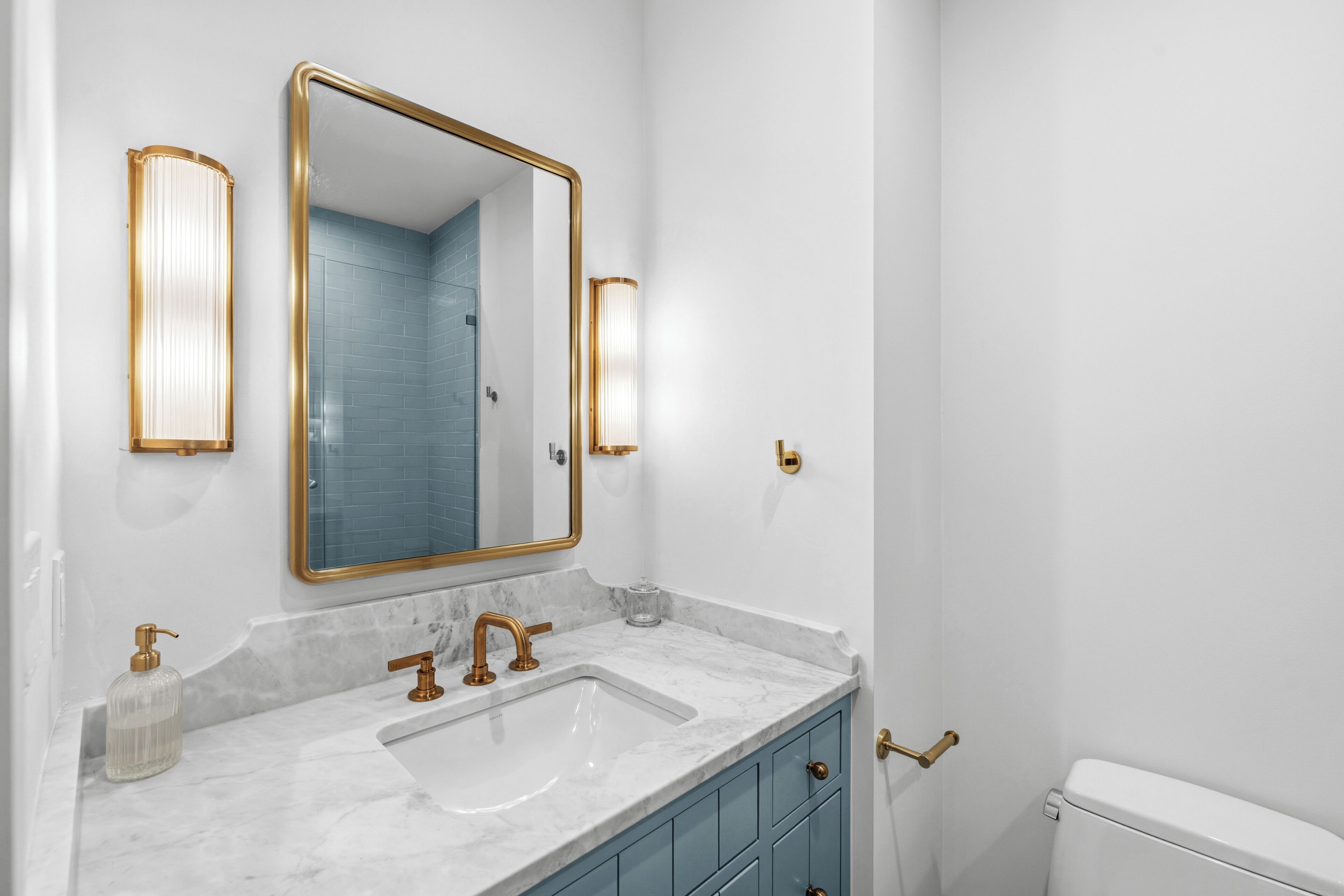 A bathroom with a white sink, gold faucets, a gold-framed mirror, and blue-tiled walls.