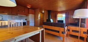 A wooden interior with a kitchen, dining table, sofa, and a fireplace.
