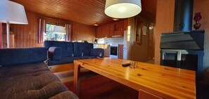 A cozy cabin interior with a wooden dining table, sofa, and kitchen area including a stove and refrigerator.