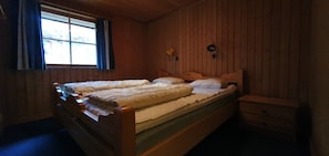 Ein Zimmer mit Holzwandverkleidung, einem Doppelbett, einem Nachttisch und zwei Wandleuchten.