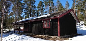 Eine kleine Holzhütte mit roter Umrandung, umgeben von Schnee und Bäumen.