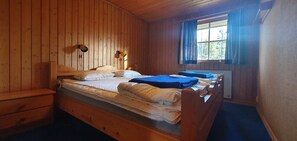 Ein Zimmer mit Holzboden, zwei Betten, einem Fenster mit Vorhängen und einem hölzernen Schminktisch.