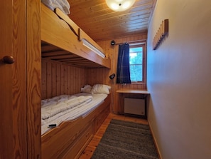 Ein gemütlicher Holzblockraum mit Etagenbetten, einem kleinen Schreibtisch und einem Fenster mit Vorhängen.
