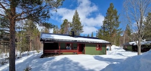 Eine Hütte mit roter Außenwand, einer Veranda und einem mit Schnee bedeckten Dach.