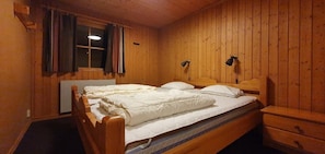 Ein Zimmer mit Holzwänden, einem Bett, Nachttischen und einem Fenster mit Vorhängen.