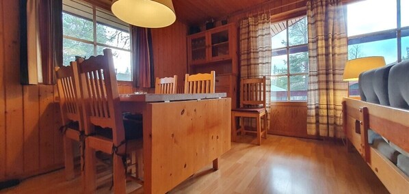 Ein Holzinterieur mit einem Esstisch, Stühlen, einer Couch und einem Fenster mit Vorhängen.