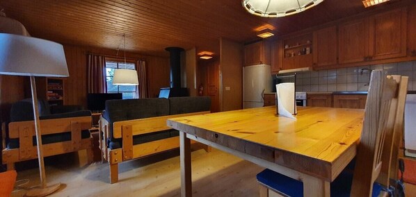 Ein Holzinnenraum mit Esstisch, Bänken, einer Couch, einem Fernseher und einer Küchenzeile.